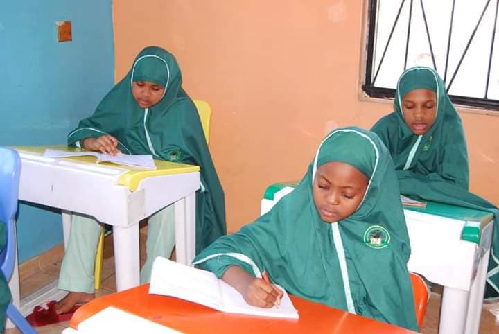 Three girls in green hijab focused on their writing in a primary classroom