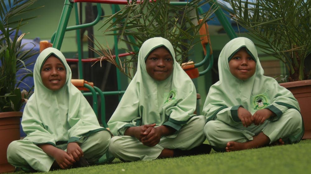Three young girls in light green hijab smiling on the school playground