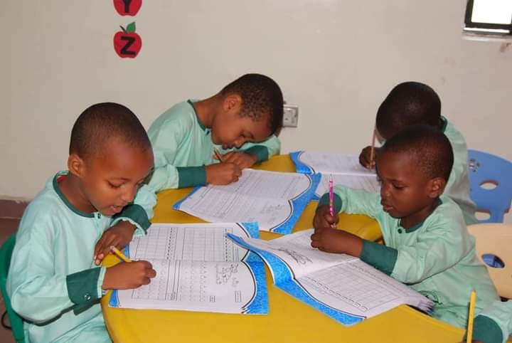 Four nursery pupils in green uniform writing together at a round table