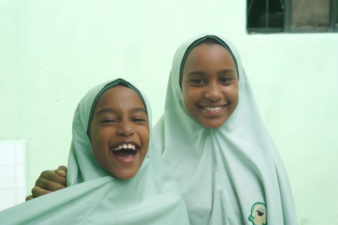 Two students in light green hijab laughing together